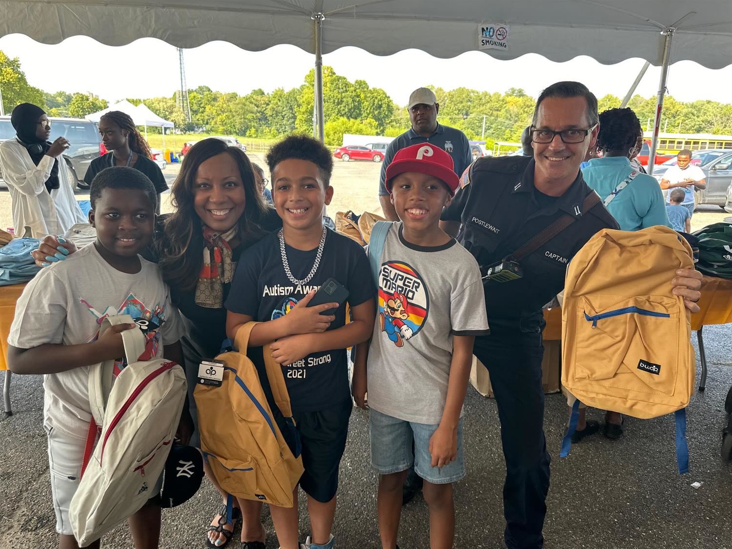 students stand with superintendent Dr. Mumin and Police Officer holding backpacks